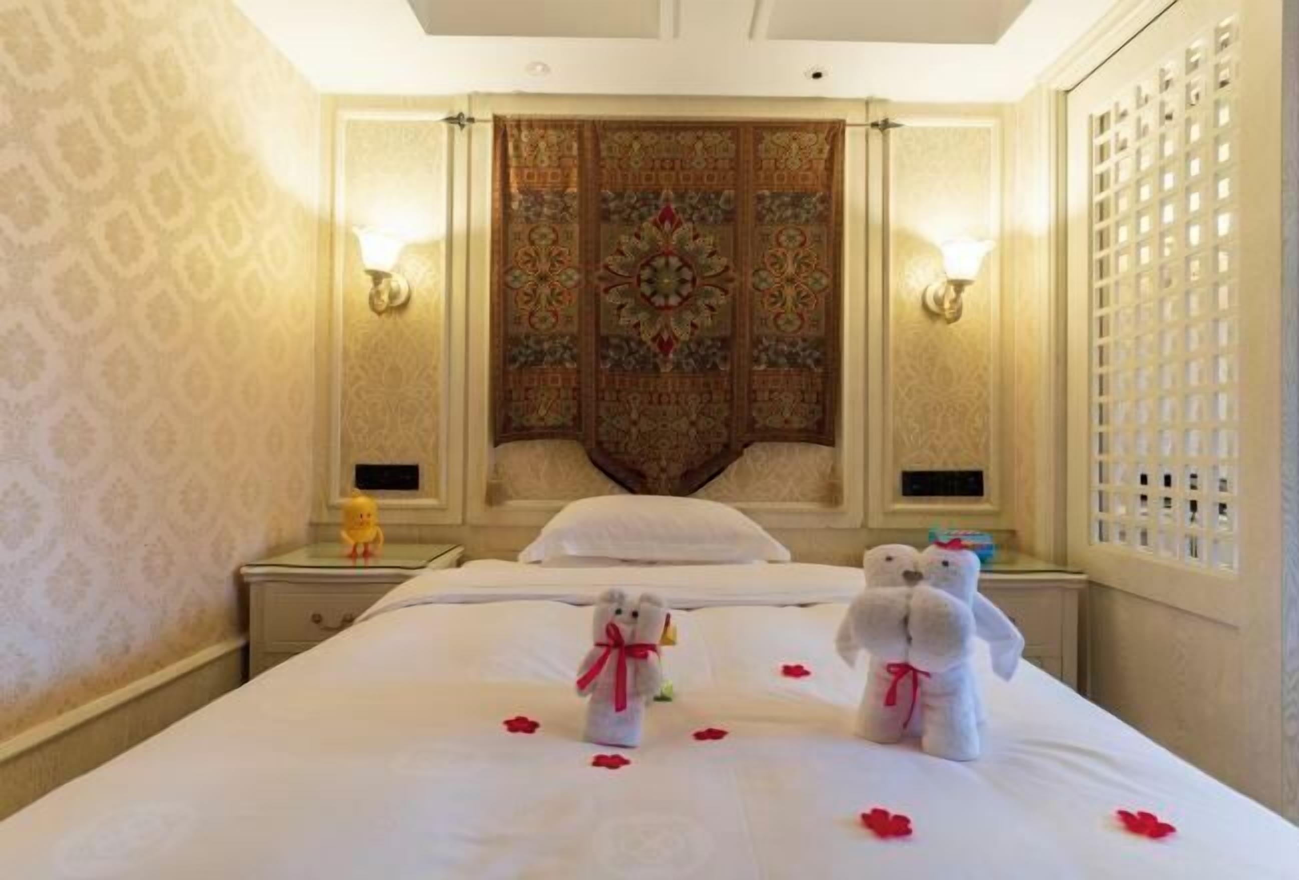 A hotel room with a large bed, two bedside tables, a decorative headboard, and a wall-mounted light fixture.