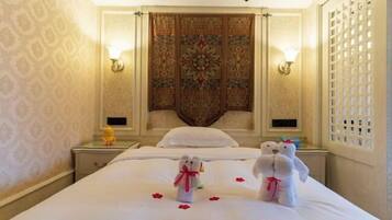 A hotel room with a large bed, two bedside tables, a decorative headboard, and a wall-mounted light fixture.