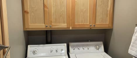 A laundry area with two white washing machines, wooden cabinets above, and a towel hanging on the wall.