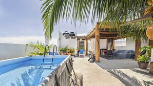 Un área de piscina en la azotea con vistas despejadas al mar, una zona de estar cubierta y plantas en macetas.