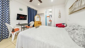 Una habitación de hotel con una cama, un escritorio, una silla, un televisor y un ventilador de techo.