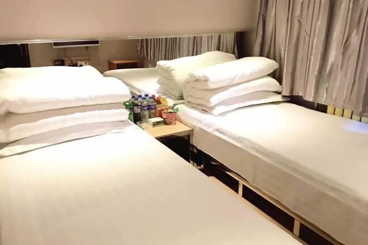 Hotellihuone, jossa on kaksi sänkyä, yöpöytä, jossa on hygieniatarvikkeita, ja verho.