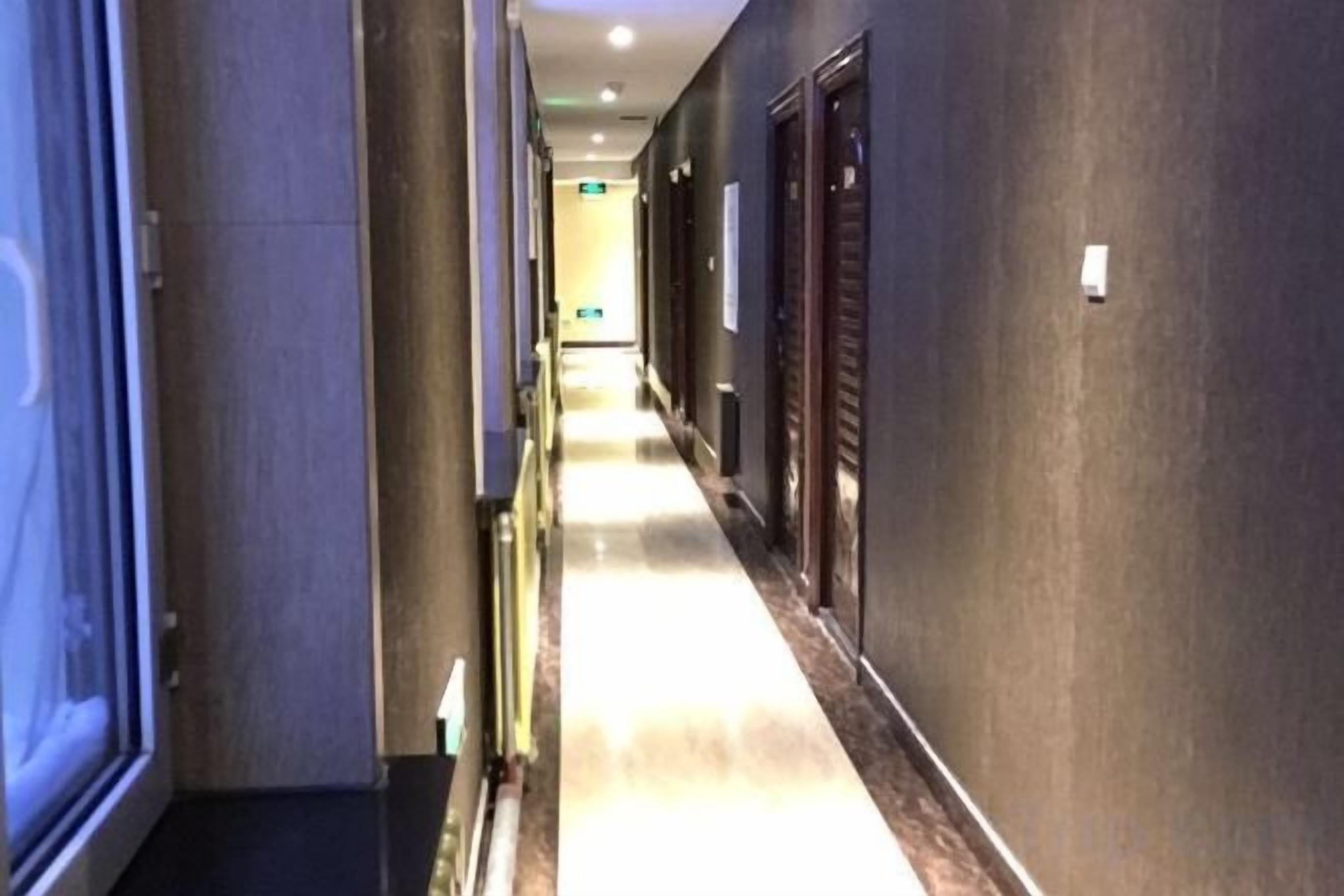 A hotel corridor with doors on both sides, a light-colored floor, and a ceiling with recessed lighting.