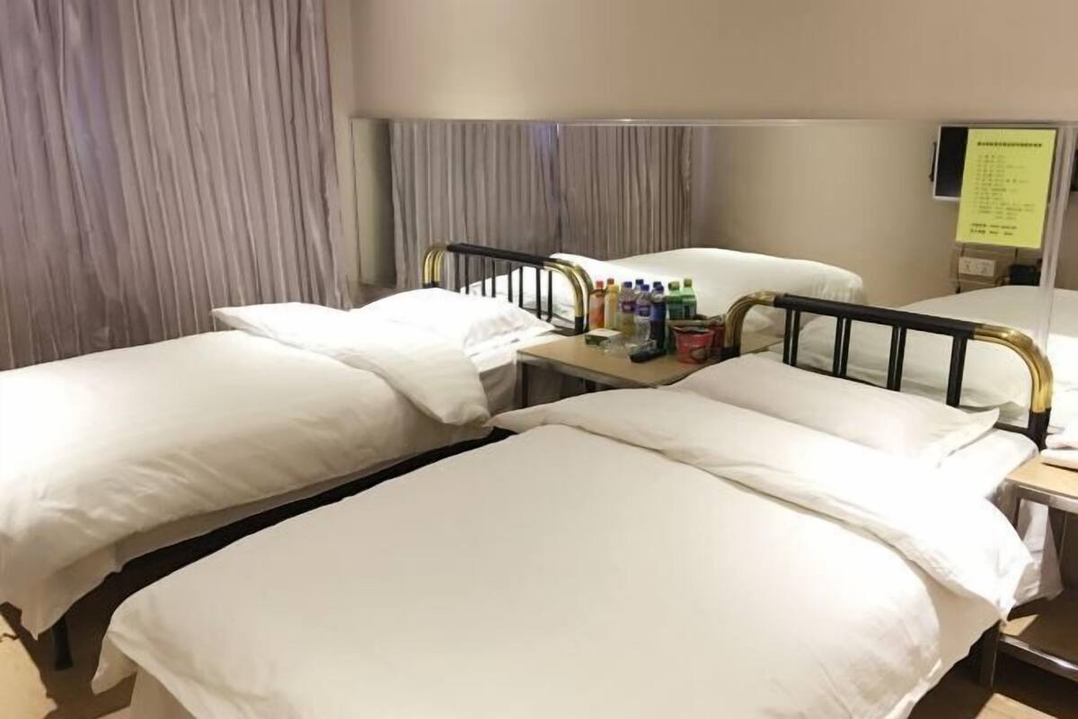 Hotellihuone, jossa on kaksi erillistä sänkyä, yöpöytä, jossa on hygieniatarvikkeita, ja verho.