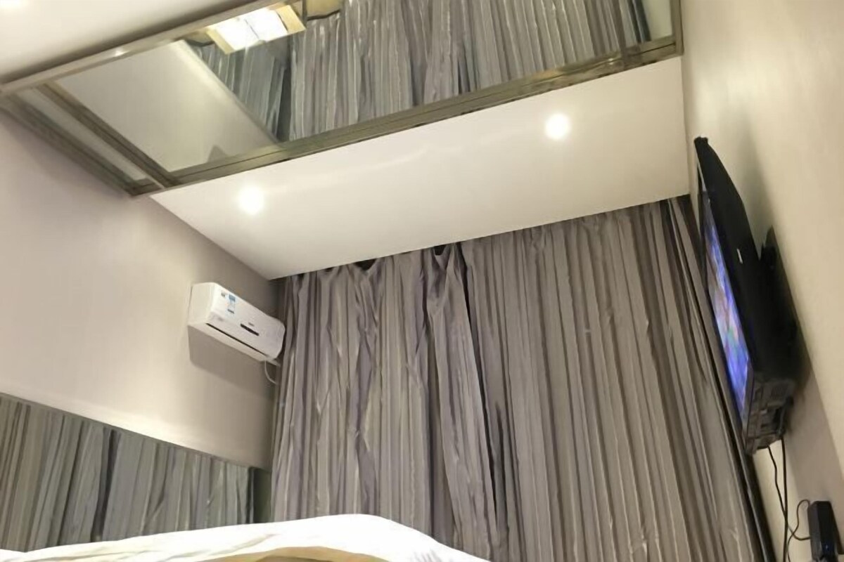 Una habitación de hotel con una cama, televisión, aire acondicionado y un espejo grande en la pared.
