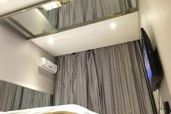 Una habitación de hotel con una cama, televisión, aire acondicionado y un espejo grande en la pared.