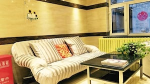 A modern living room with a striped sofa, a glass coffee table, and a window with a view of the city. - Friendship City New Town Hotel (Youyi)