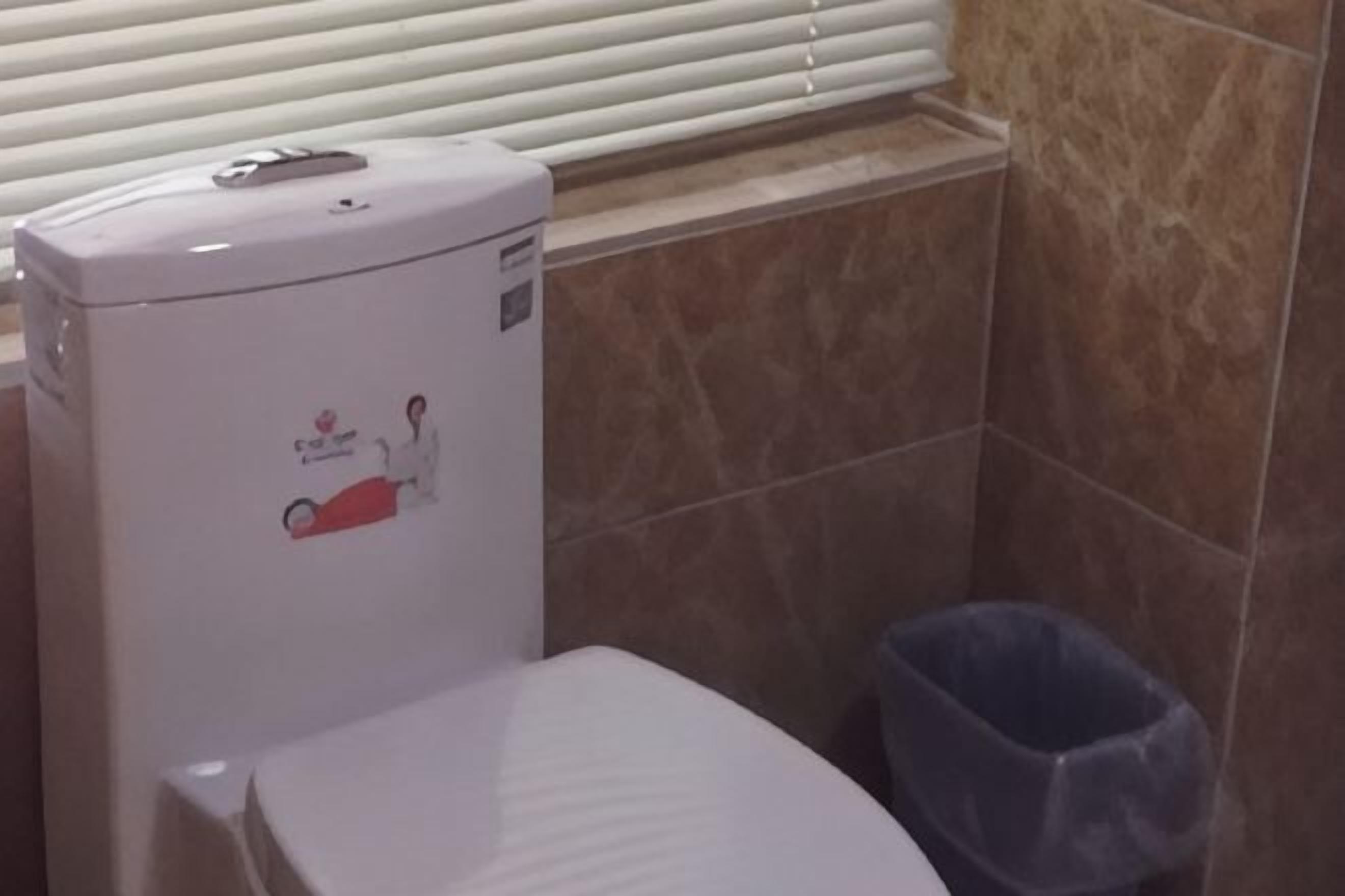 Un baño con inodoro, un bote de basura y una ventana con persianas.