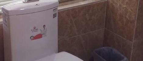 Un baño con inodoro, un bote de basura y una ventana con persianas.