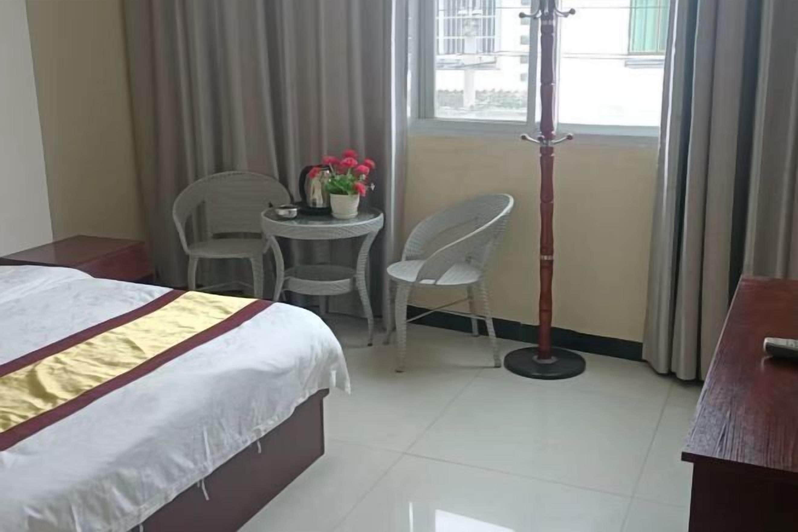 A hotel room with a bed, a small table with flowers, a chair, and a tall floor lamp.