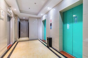 A hotel corridor with a tiled floor, a trash bin, and a green elevator door.