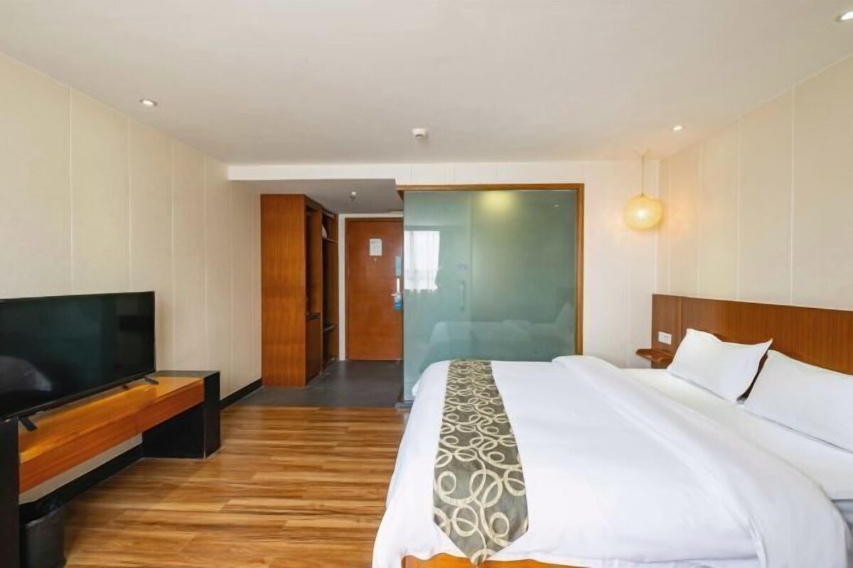 Habitación de hotel con cama, televisión, piso de madera y un pasillo que conduce a otra habitación.