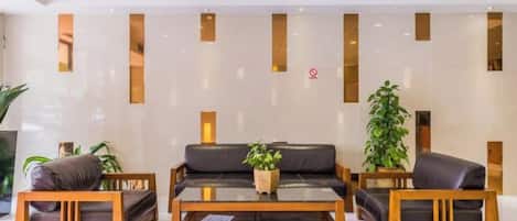 A reception area with a sofa, two wooden chairs, a coffee table, and a potted plant.