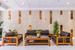 A reception area with a sofa, two wooden chairs, a coffee table, and a potted plant. - Weistin Hotel (Taishan)