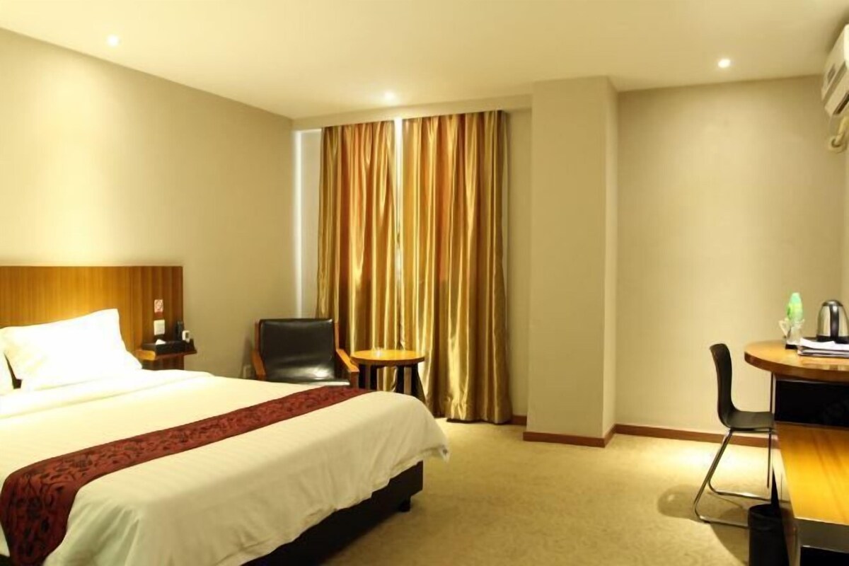 A hotel room with a bed, a desk, a chair, a small table, and a curtain.