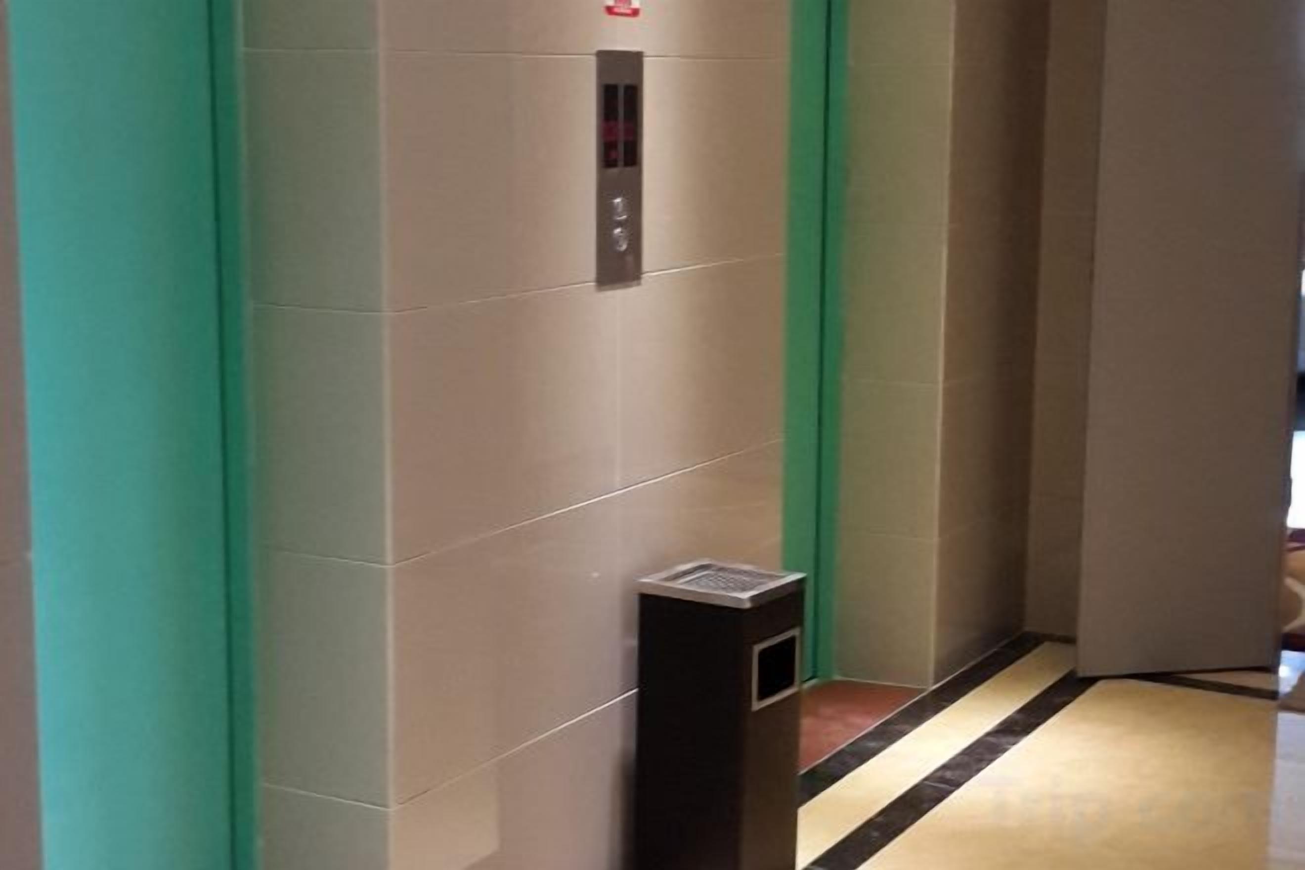 Corredor com elevador embutido na parede e uma lixeira.