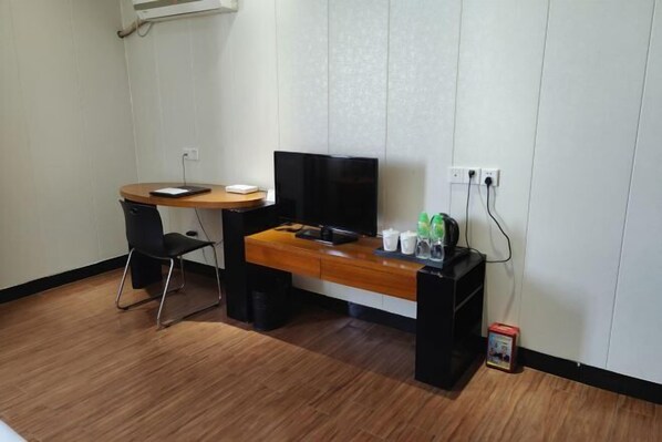 Una habitación pequeña con un escritorio de madera, una silla negra, un televisor y un mueble bajo con botellas.