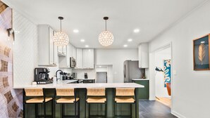 A modern kitchen with a central island, bar stools, pendant lighting, and a view to the dining area.