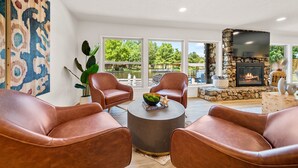 A living room with leather chairs, a round coffee table, a fireplace, and large windows.