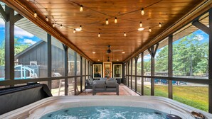 A covered outdoor hot tub area with a wooden ceiling, seating, and a view of the surrounding landscape.