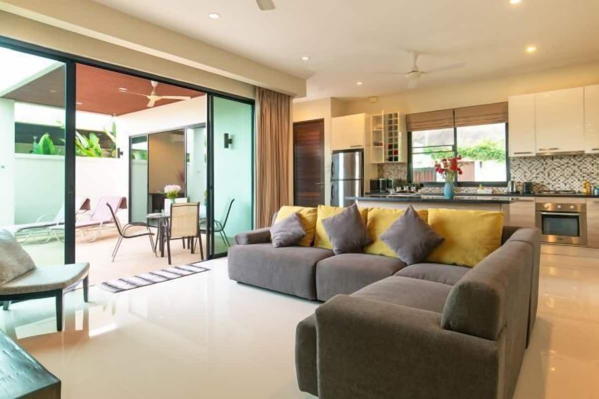 A modern living room with a sofa, a dining area, and a kitchen with cabinets and appliances.