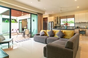 A modern living room with a sofa, a dining area, and a kitchen with cabinets and appliances. - Andaman 3Br Pool Villa （IV2V7） (Phuket)