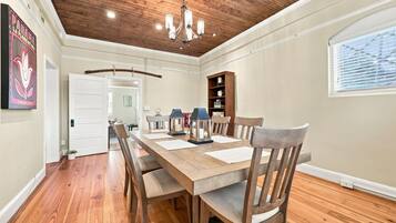 Un coin repas avec une table et des chaises en bois, un lustre et une bibliothèque.