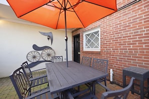 An outdoor patio with a wooden table and chairs, an orange umbrella, and decorative metal elements.