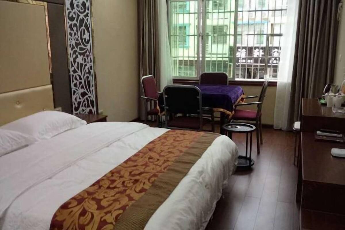 Een hotelkamer met een bed, een bureau met stoel, een klein tafeltje en een raam met uitzicht op gebouwen.
