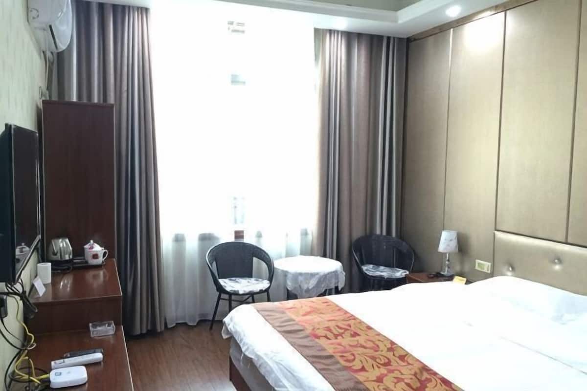 Een hotelkamer met een bed, een bureau met stoel, een klein tafeltje, een televisie en gordijnen.