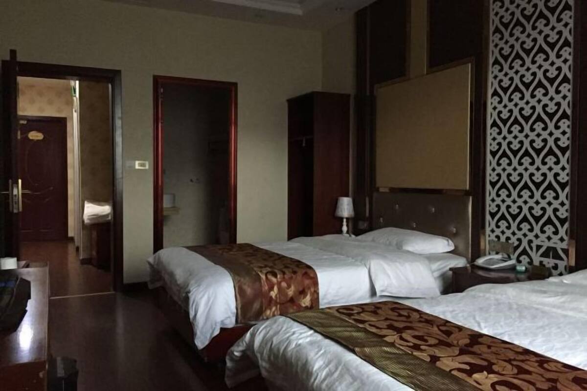 Een hotelkamer met twee bedden, een kledingkast, een nachtkastje en een behang met patroon.