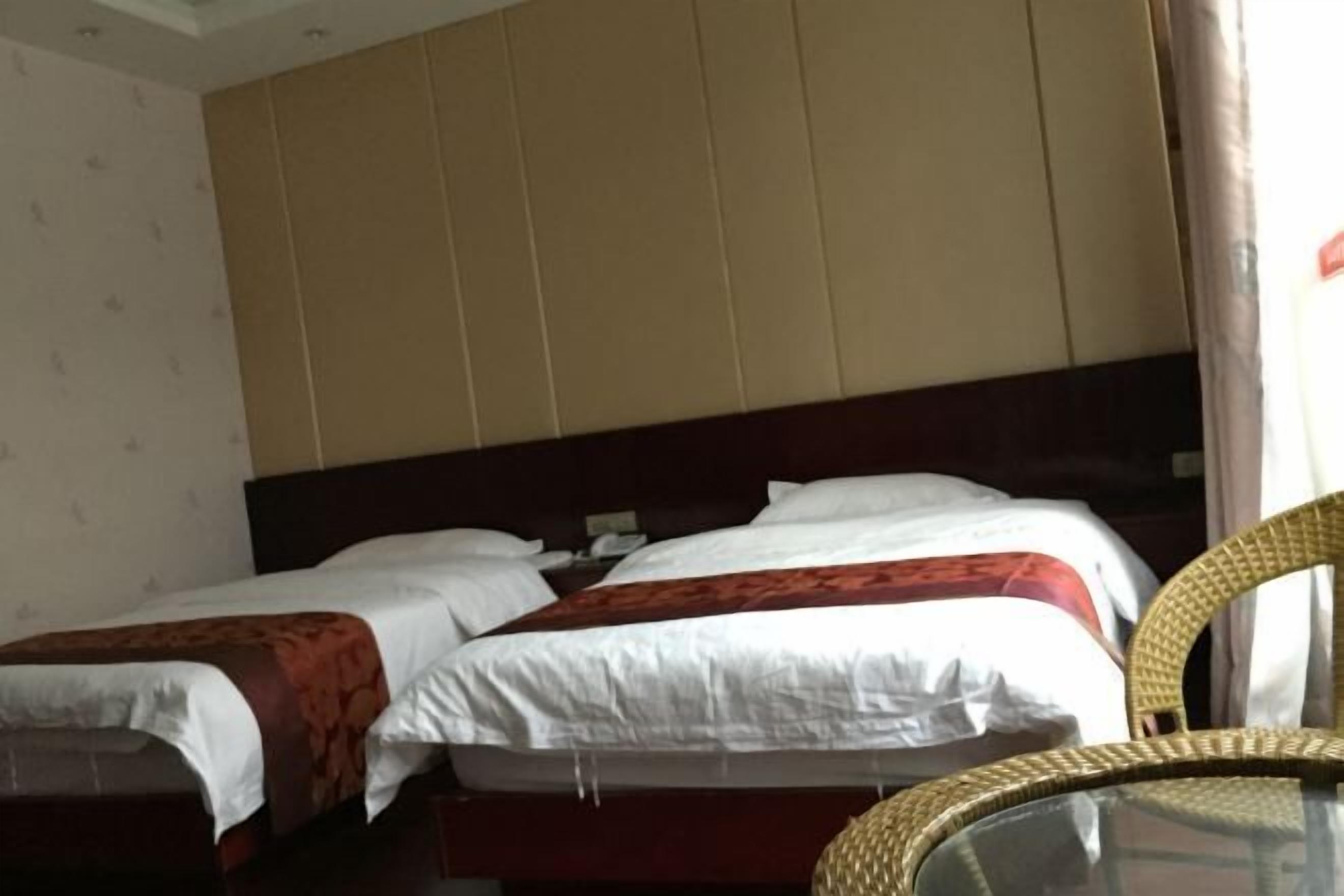 Een hotelkamer met twee bedden, een houten hoofdbord en een rieten stoel.