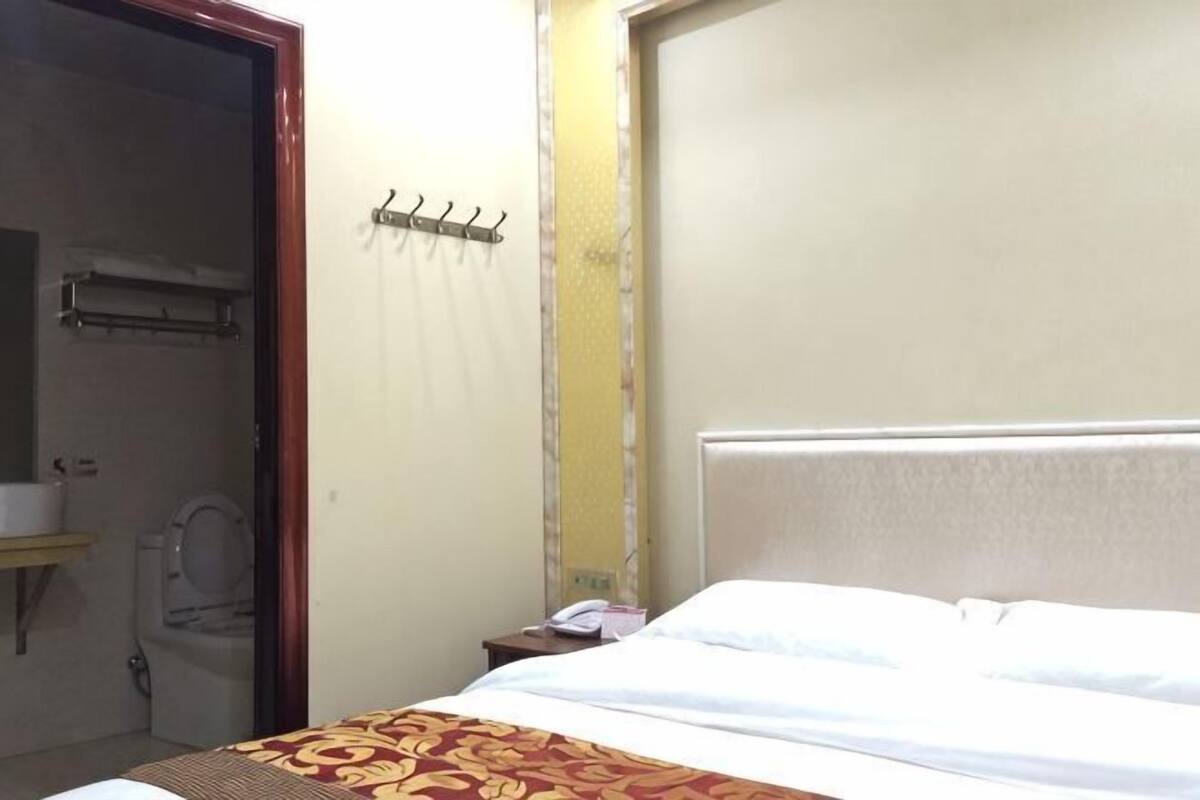 Een hotelkamer met een bed, een nachtkastje, een badkamer met toilet en wastafel, en een raam met gordijn.