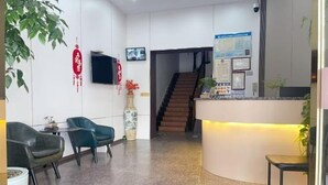 A reception area with a curved desk, two chairs, a staircase, and a wall-mounted TV. - Minfeng Hotel (Yueqing)