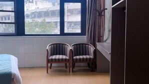 A room with a bed, two striped chairs, a window with a view of buildings, and a dark-colored wardrobe. - Minfeng Hotel (Yueqing)