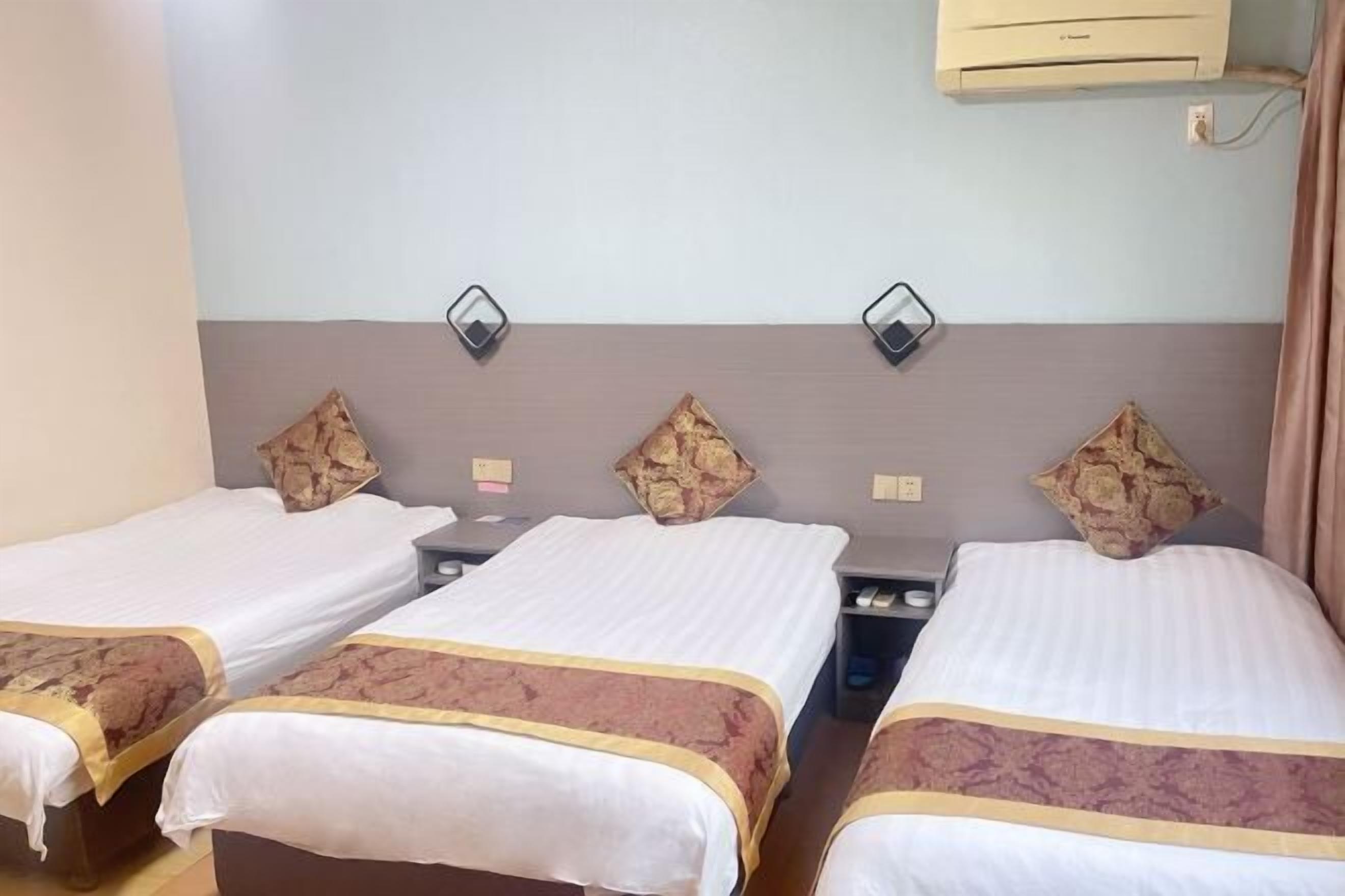A hotel room with two single beds, a bedside table, a wall-mounted air conditioner, and a curtain.