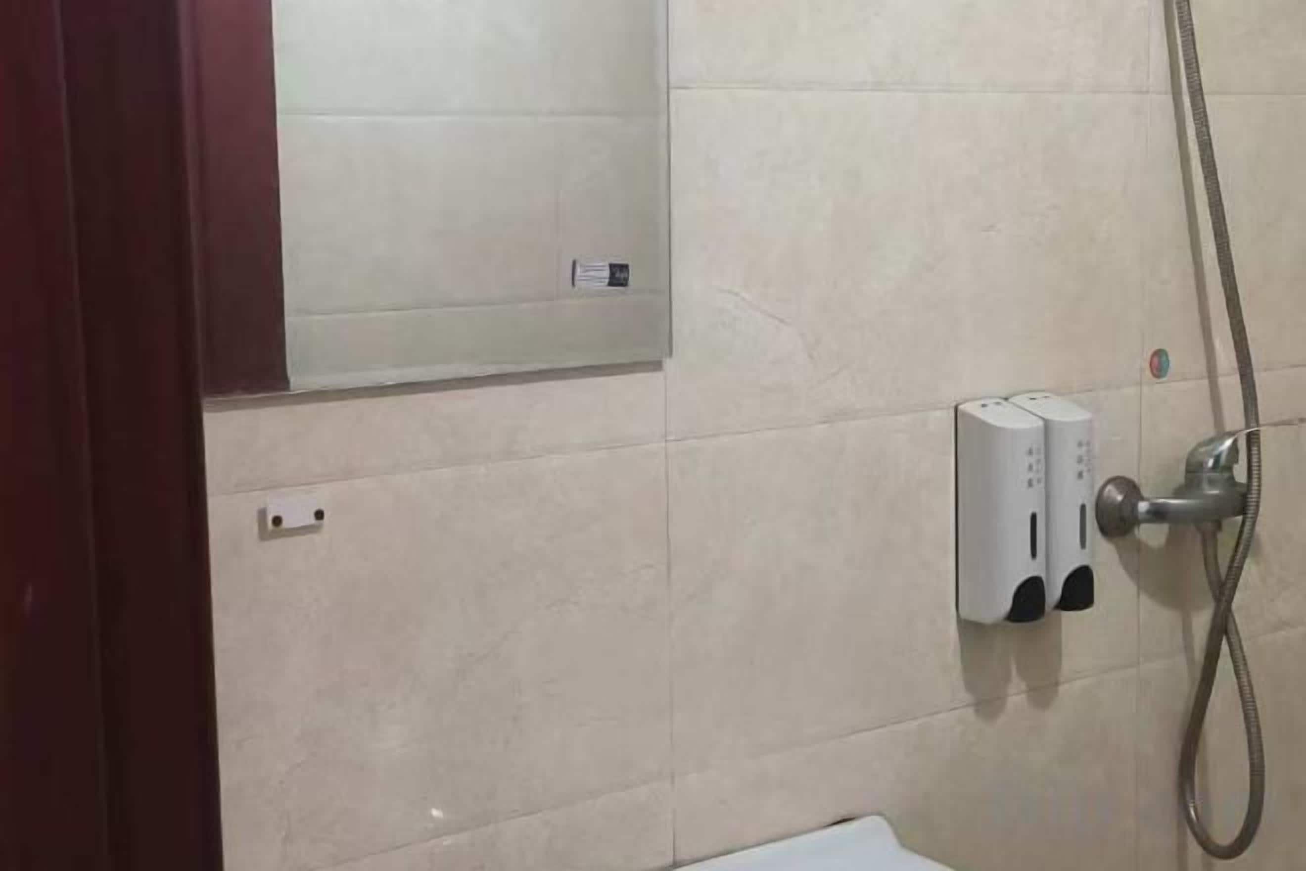 A bathroom with a wall-mounted mirror, a towel dispenser, and a showerhead.