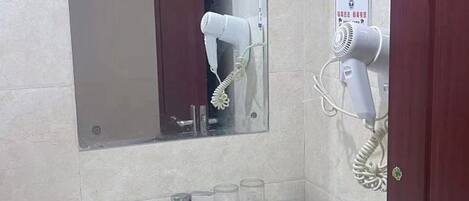Un baño con lavamanos, espejo y dos secadores de pelo montados en la pared.