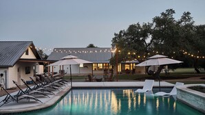 Una piscina con sillones de descanso y sombrillas, rodeada de edificios y árboles.