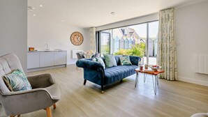 A modern living room with a sofa, a chair, a dining table, and a kitchen area in the background. - 2 Bed in Woolacombe (oc-b27615) (Woolacombe)