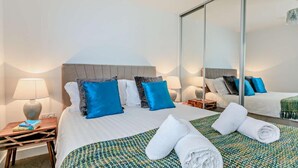 A hotel room with a bed, two bedside tables, a mirror, and a view of the outside. - 2 Bed in Woolacombe (oc-b27615) (Woolacombe)