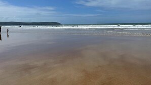 A beach with a wet sand foreground, a clear sky, and distant hills. - 2 Bed in Woolacombe (oc-b27615) (Woolacombe)