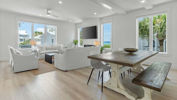 A spacious living area with a wooden dining table, white sofas, and a flat-screen TV mounted on the wall.