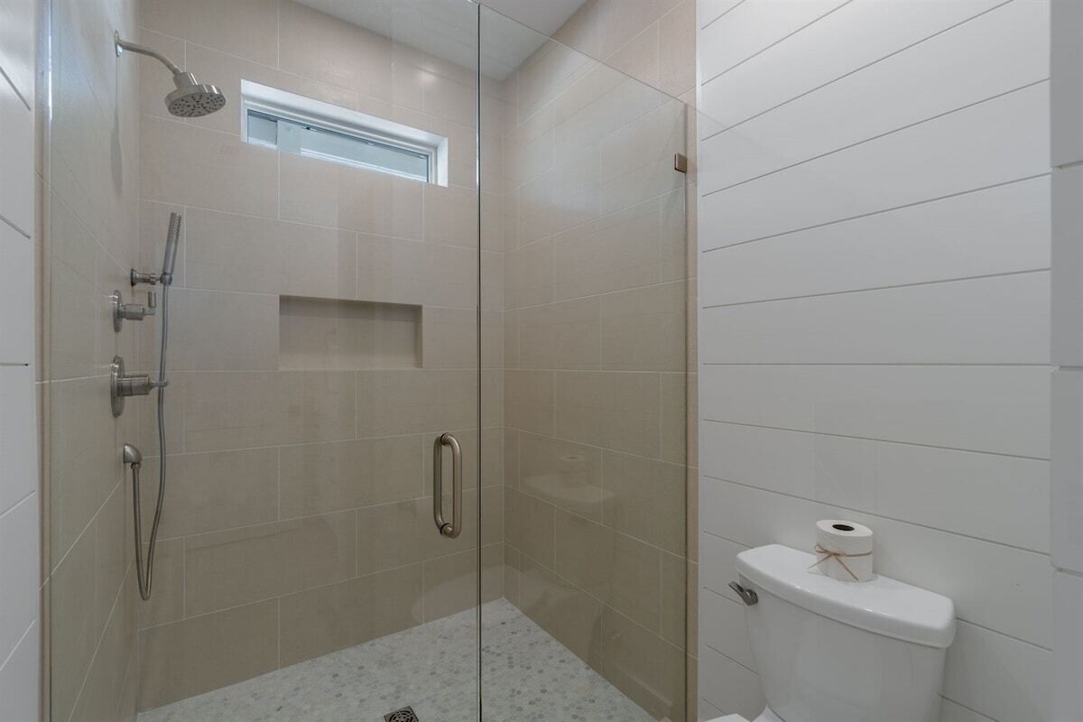 A glass-enclosed shower area with a showerhead, handheld shower, and a small window above the shower.