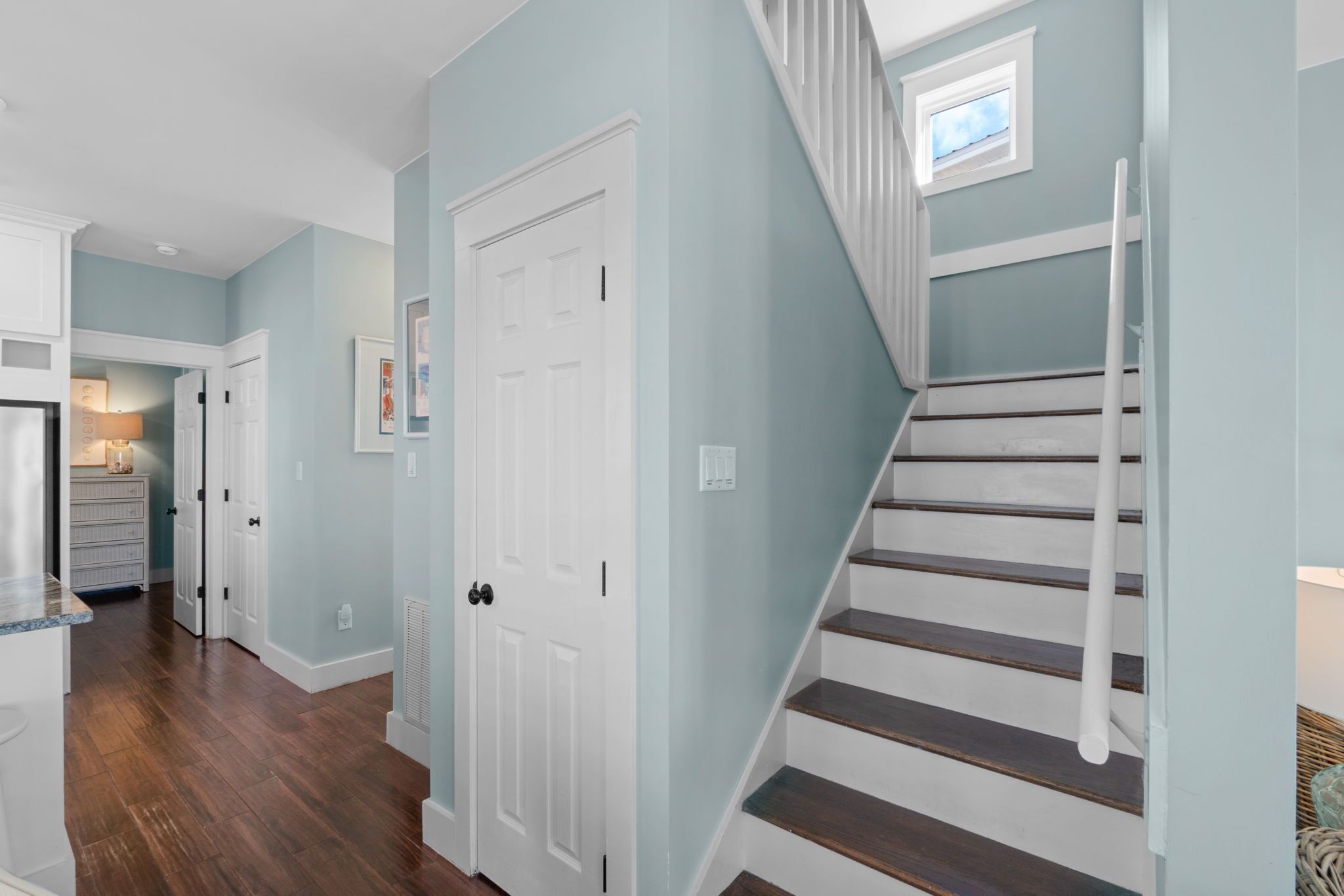 A hallway with a staircase, white doors, and a kitchen area visible in the background.