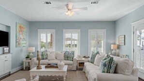 A living room with a ceiling fan, white sofas, a coffee table, and a TV. - Ocean front: Private Pool + Private Beach Access (Seagrove Beach)