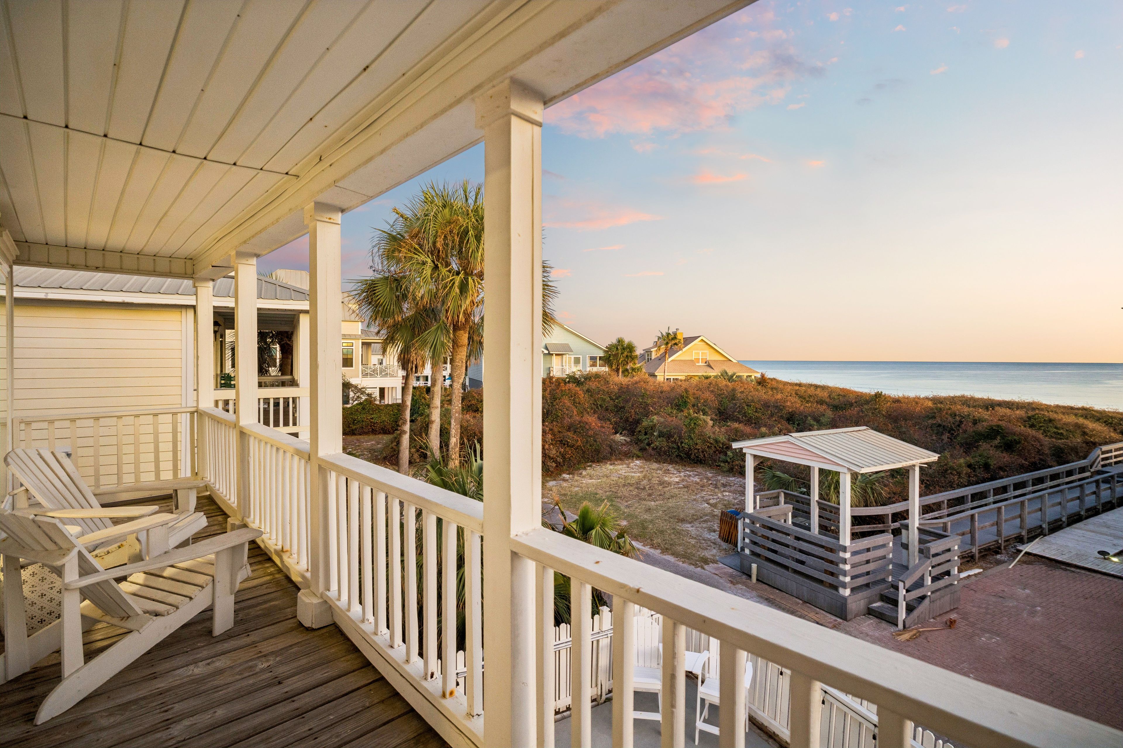 A wooden deck with chairs and a gazebo overlooking a beach.