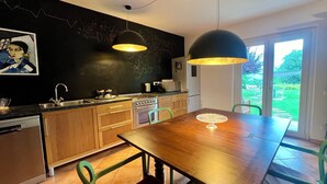 A modern kitchen with a wooden table, green chairs, and a large window.