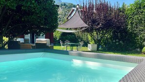 A swimming pool with clear water, surrounded by a patio area with outdoor furniture and a pergola providing shade.