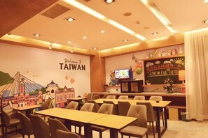 A restaurant with tables and chairs, a wall with a 'Welcome to Taiwan' sign, and a television screen. - Newful Hotel (Taipei)